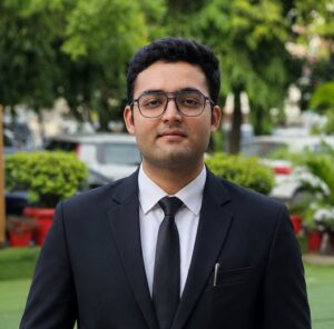 A man in a black suit and tie holding a brown leather-bound notebook labeled 'Legal Briefs' outdoors in a park.