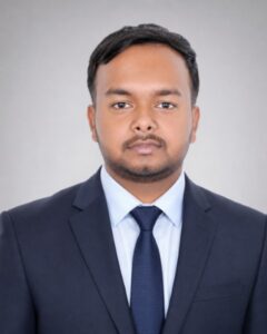 Professional headshot of a man in a dark suit and blue tie against a neutral gray background, looking at the camera.